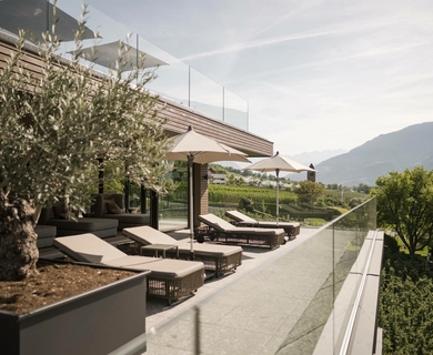 Dachterrasse mit Liegen im Wellnesshotel Naturns Auf der Dachterrasse stehen Liegen und Sonnenschirme mit Blick auf die Berge.