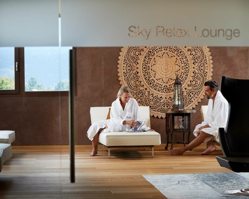 Two guests in bathrobes sit in the Sky Relax Lounge and relax on lounge furniture.