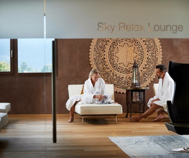 Two guests in bathrobes sit in the Sky Relax Lounge and relax on lounge furniture.