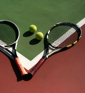 Two tennis rackets and two yellow balls lie on a tennis court with green and red surfaces.