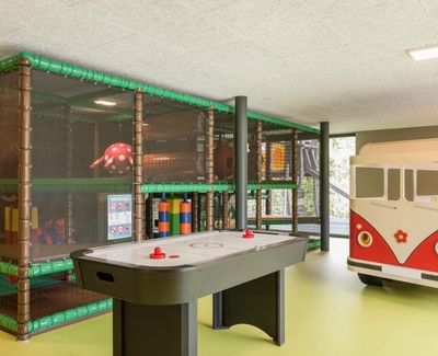 Ein Indoor-Spielbereich mit Airhockey-Tisch, Kletterstruktur und Spielbus für Kinder.