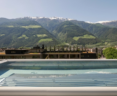 Poolterrasse mit Bergblick im Feldhof Resort Der Pool auf der Terrasse liegt vor einer Bergkulisse mit grünen Hängen und schneebedeckten Gipfeln.