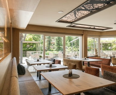 Hotelrestaurant im Feldhof DolceVita Resort Ein heller Restaurantbereich mit Holztischen, Polsterbänken und großen Fensterfronten zum Garten.
