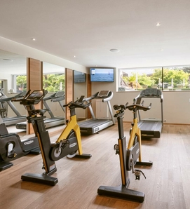 Ein heller Fitnessraum mit mehreren Ergometern und Laufbändern vor großen Fenstern.