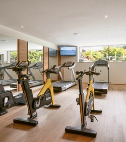 Ein heller Fitnessraum mit mehreren Ergometern und Laufbändern vor großen Fenstern.