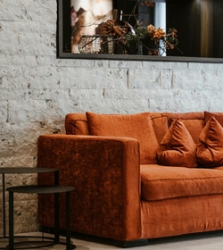 Ein orangefarbenes Loungesofa mit Kissen steht vor einer hellen Steinwand.