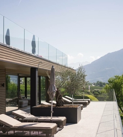 Lettini e ombrelloni sono disposti sulla terrazza con parapetto in vetro e vista sulle montagne.