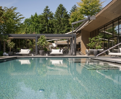 Pool im Wellnesshotel Feldhof in Naturns Ein Außenpool mit Liegen und Pergola neben dem modernen Hotelgebäude.