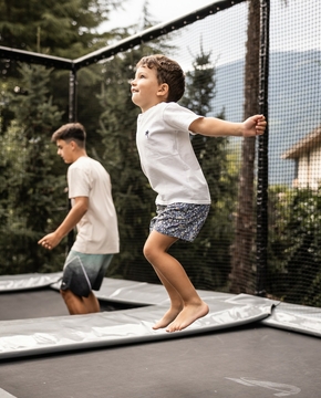 Drei Kinder springen gemeinsam auf einem Trampolin im Garten vor dem Hotel.
