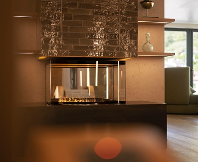 Kamin im Ruheraum des Feldhof DolceVita Resort Ein moderner Kamin steht in einem ruhigen Aufenthaltsbereich mit Fenster und Regalen.