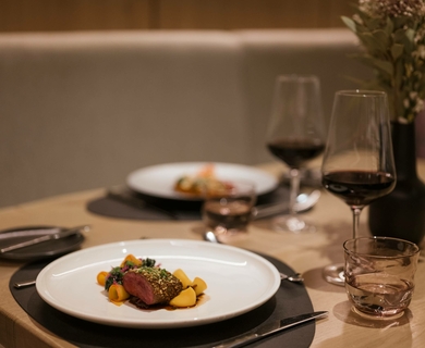 Feines Dinner im Hotelrestaurant in Naturns Ein gedeckter Tisch mit zwei Tellern, Weingläsern und einem angerichteten Teller im Hotelrestaurant.