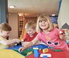 Drei Kinder spielen gemeinsam an einem Tisch mit Bausteinen in der Kinderbetreuung.