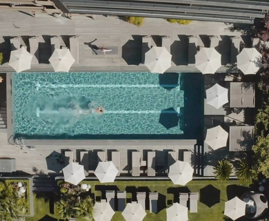 Pool mit Sonnenschirmen im Feldhof DolceVita Resort Blick auf den Poolbereich mit Sonnenliegen, weißen Schirmen und einer einzelnen Person im Wasser.