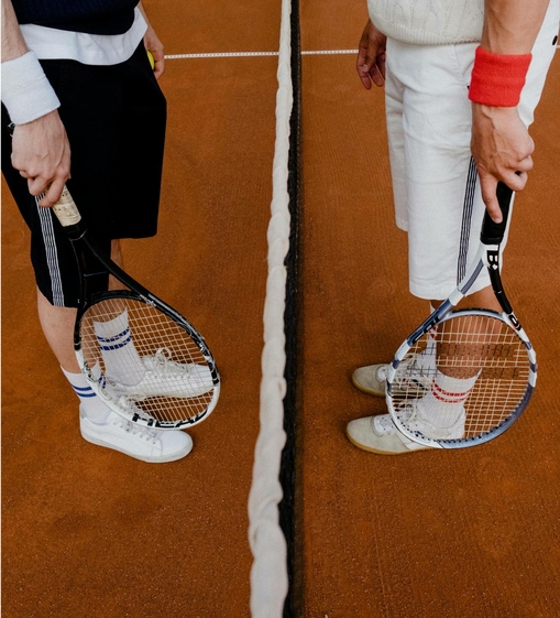 Two tennis players stand with rackets at the net on an indoor court.