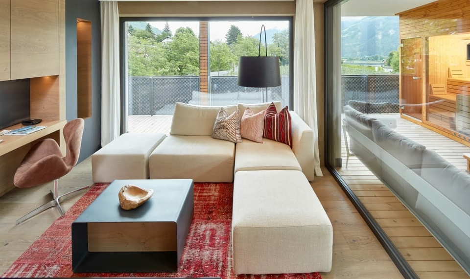 Chalet mit Loggia, Sauna und Whirlpool Ein heller Wohnbereich im Chalet mit Sofa, Teppich und Blick auf die Loggia mit Sauna und Whirlpool.