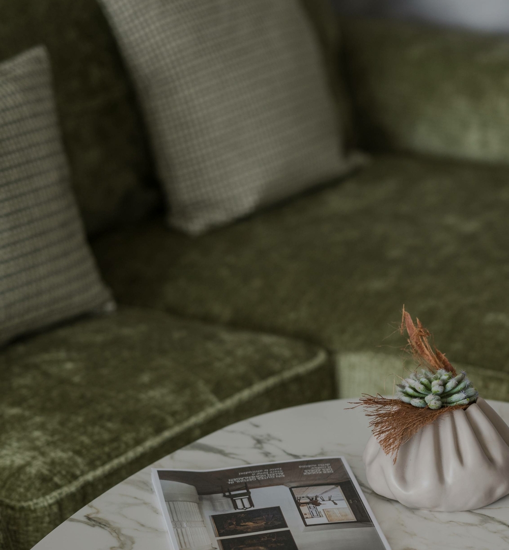 Ein grünes Sofa und ein Marmortisch mit Dekoration in einem ruhigen Sitzbereich.