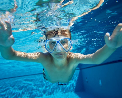 Ein Kind schwimmt unter Wasser mit Taucherbrille im Pool.