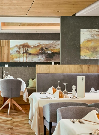 A stylish hotel restaurant area with white tablecloths, upholstered chairs, and artwork on the wall.