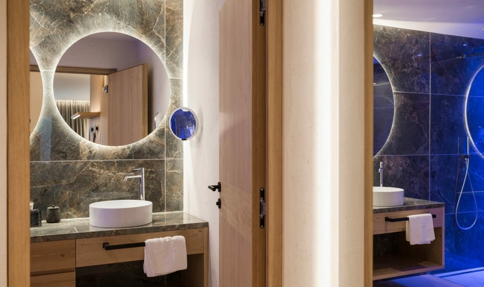Badezimmer im Doppelzimmer La Vita in Naturns Ein modernes Badezimmer mit runder Spiegelwand, Aufsatzwaschbecken und Holzdetails im Doppelzimmer La Vita.