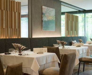 Restaurant im Hotel Feldhof in Naturns Eingedeckte Tische und Stühle in einem eleganten Hotelrestaurant mit Holzlamellen und Spiegelwand.