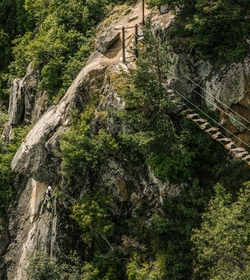 Ein Kletterer bewegt sich an einer steilen Felswand neben einem Klettersteig mit Holzstegen.