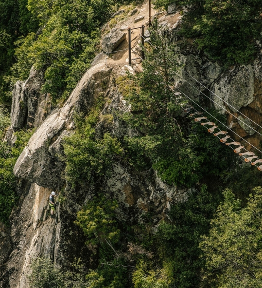 Ein Kletterer bewegt sich an einer steilen Felswand neben einem Klettersteig mit Holzstegen.