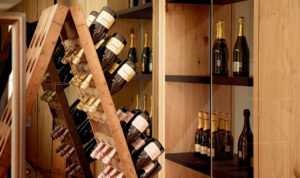 Ein Holzregal im Weinkeller zeigt mehrere Flaschen mit Wein und Sekt hinter Glas.