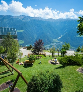 Un giardino curato dell'hotel con lettini, area giochi e ampia vista sulla valle e sulle montagne.