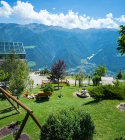 Un giardino curato dell'hotel con lettini, area giochi e ampia vista sulla valle e sulle montagne.