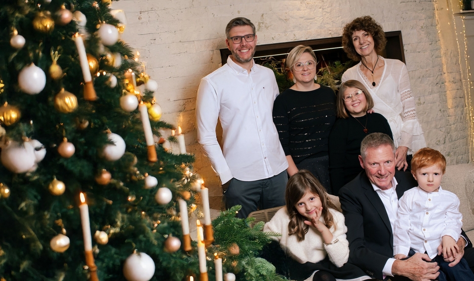 Sechs Personen stehen und sitzen neben einem festlich geschmückten Weihnachtsbaum in Innenräumen.