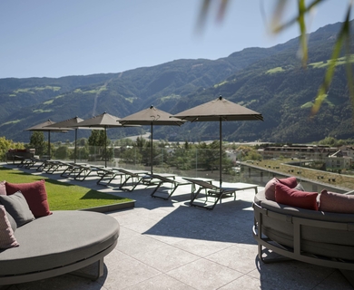 Panoramaterrasse mit Liegen im Feldhof Resort Eine Panoramaterrasse mit Liegen, Sonnenschirmen und Blick auf die Berge.