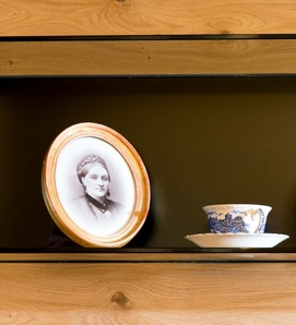 Ein gerahmtes Schwarz-Weiß-Porträt steht neben einer Teetasse und Untertasse im Holzregal.