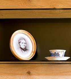 Ein gerahmtes Schwarz-Weiß-Porträt steht neben einer Teetasse und Untertasse im Holzregal.