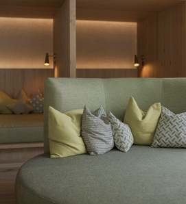 Una lounge accogliente con sedute imbottite, cuscini e luce calda al Feldhof DolceVita Resort.