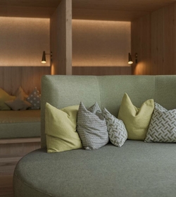 Una lounge accogliente con sedute imbottite, cuscini e luce calda al Feldhof DolceVita Resort.