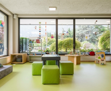 Kinderbetreuung im Family Spa des Feldhof Ein heller Kinderraum mit Spieltisch, Sitzwürfeln und großen Fenstern mit Blick ins Grüne.
