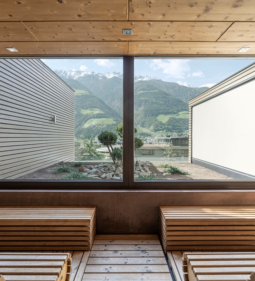 Two wooden benches in a sauna with a large window and mountain views outside.