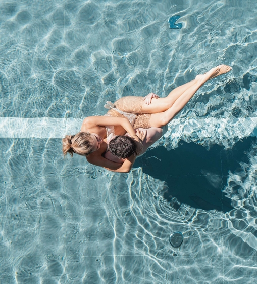 Una coppia si rilassa nell’acqua limpida della piscina, vista dall’alto.