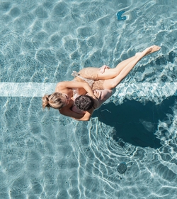 Una coppia si rilassa nell’acqua limpida della piscina, vista dall’alto.