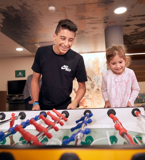 Ein Junge und ein Mädchen spielen gemeinsam Tischfußball im Innenbereich.
