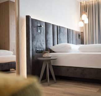 Ein modernes Hotelzimmer mit Doppelbett, Nachttisch und Vorhang im Feldhof DolceVita Resort.