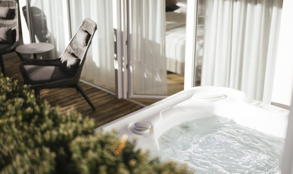 Whirlpool auf dem Balkon der Suite Bergzauber Ein Whirlpool auf dem Balkon mit Lounge-Sesseln und Blick durch helle Vorhänge ins Zimmer.
