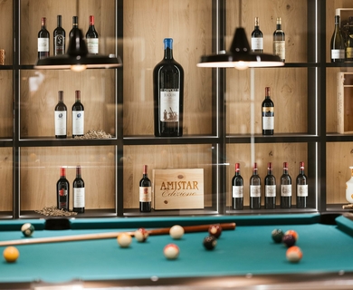 Billardraum mit Weinauswahl im Feldhof DolceVita Resort Ein Billardtisch steht vor einer Holzvitrine mit Weinflaschen im Feldhof DolceVita Resort.
