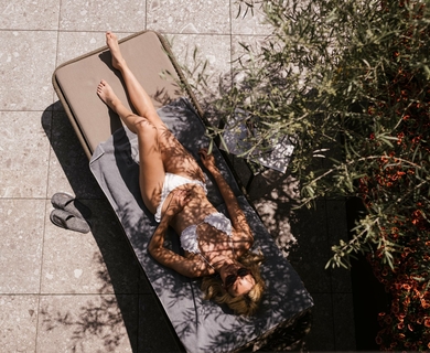Liegefläche am Pool im Wellnesshotel in Naturns Eine Frau entspannt auf einer Liege neben Pflanzen auf der Terrasse.