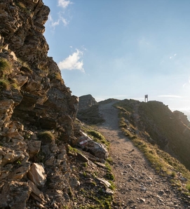 Ein schmaler Wanderweg führt entlang eines felsigen Hangs unter blauem Himmel.