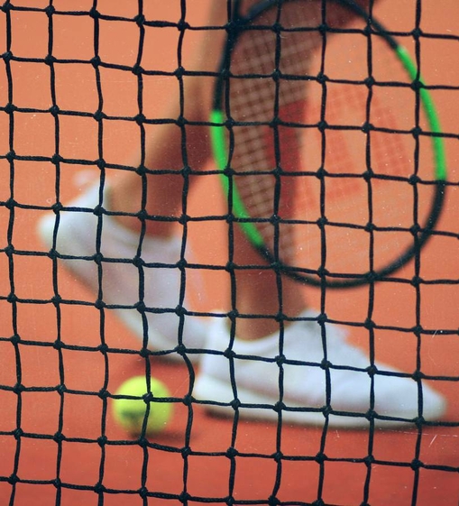 A tennis ball and racket are visible behind the net on a red court.