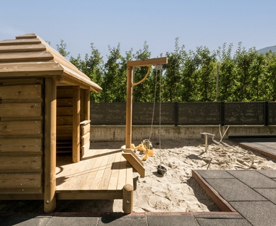 Sauna mit Sandbereich im Feldhof Resort Eine kleine Holzsauna steht neben einem Sandbereich mit Wasserstelle und Liegefläche im Außenbereich.