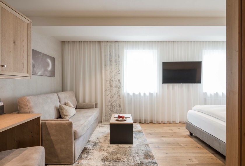 La camera doppia Silbermond mostra un angolo salotto, mobili in legno, pavimento in legno e un letto vicino alle finestre.