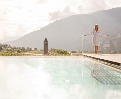 Infinity Pool mit Bergblick im Feldhof Resort Eine Frau steht am Rand des Infinity-Pools mit Blick auf die Berge und das Tal.