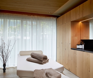Un lettino wellness bianco con asciugamani piegati si trova davanti a tende chiare nella sala relax.